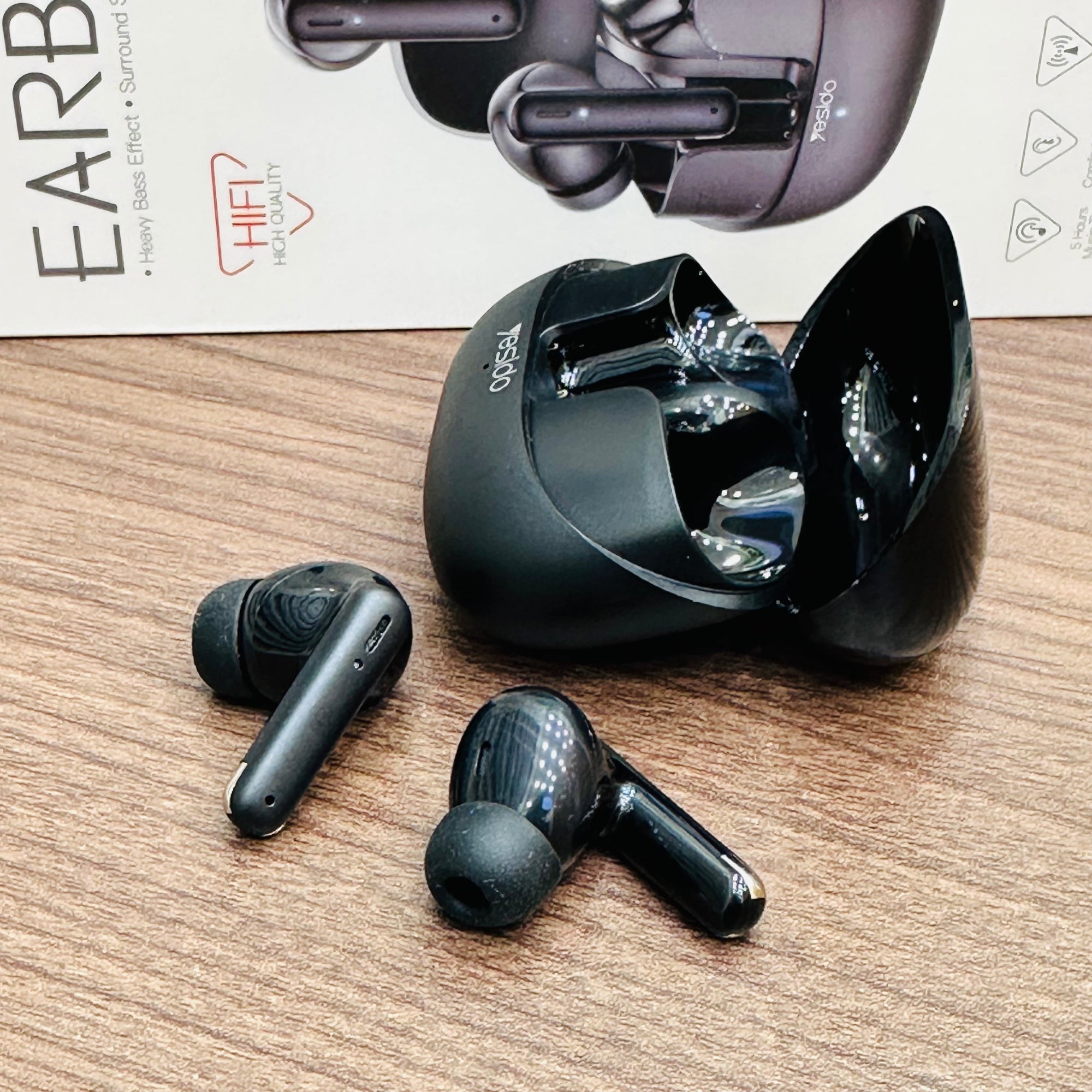 Black wireless earbuds on a wooden surface with a box in the background.
