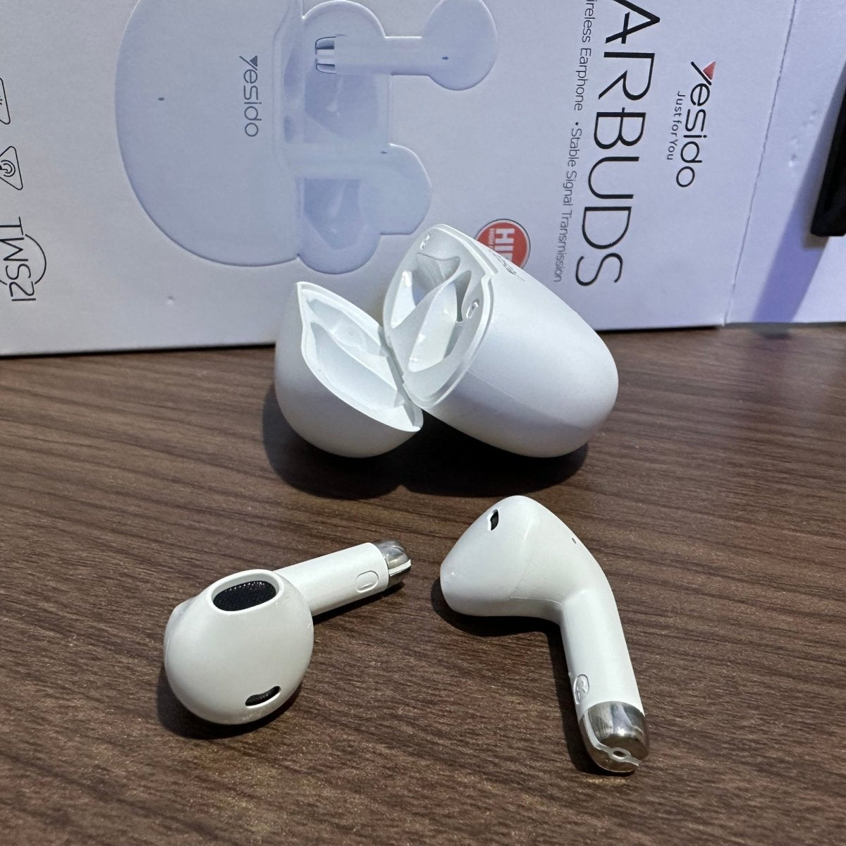 White wireless earbuds with charging case on a wooden surface, with 'yesido' branding in the background.