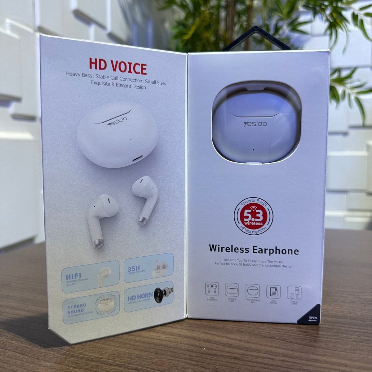 Open box of wireless earphones with product images and text on a wooden surface.