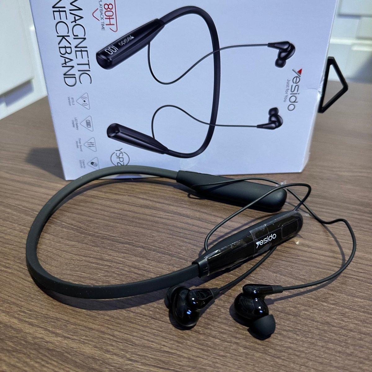 Black magnetic neckband with earpieces on a wooden surface, brand 'yesido' visible