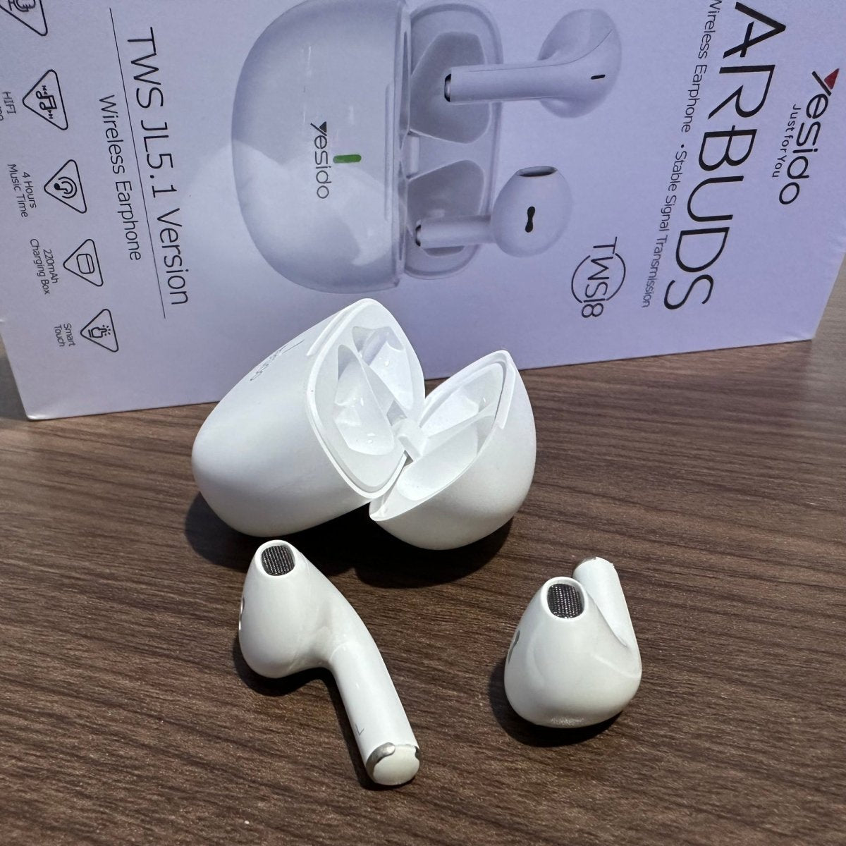 White wireless earbuds with charging case on a wooden surface, with 'AirBuds' packaging in the background.