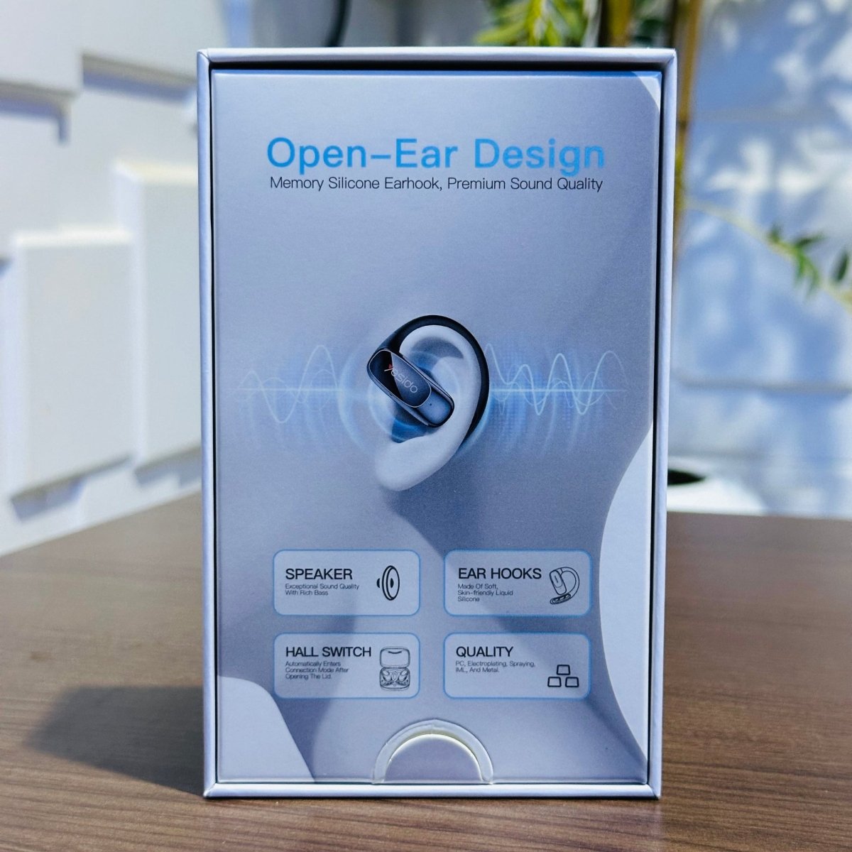 Box of open-ear design earbuds on a wooden surface with a blurred background