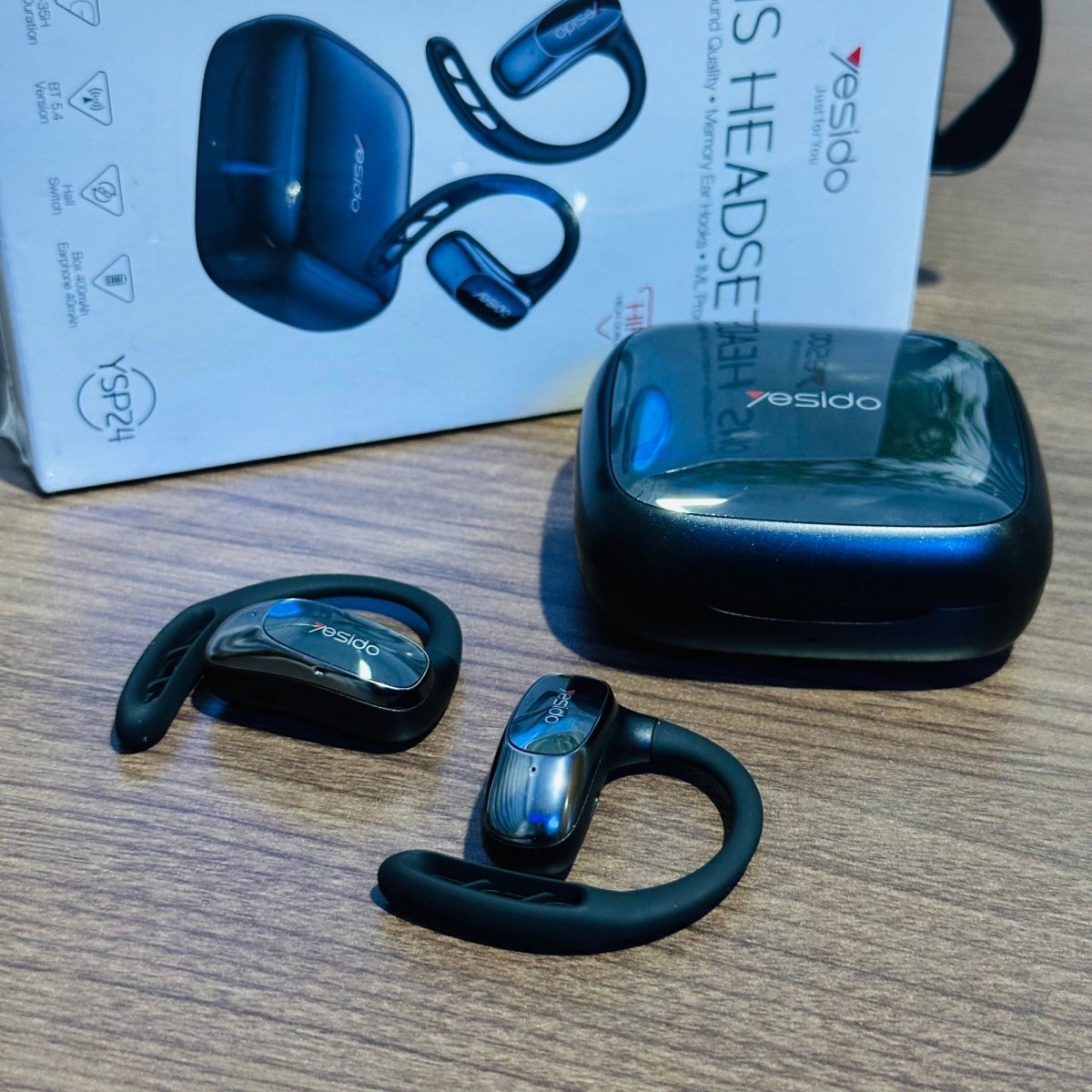Black wireless earbuds with charging case on a wooden surface, featuring the brand 'YESIDO'.