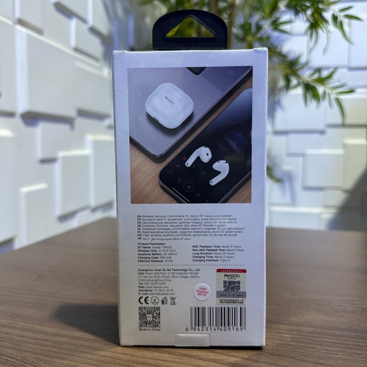 Box packaging of wireless earbuds with a phone and earbuds on a wooden surface.