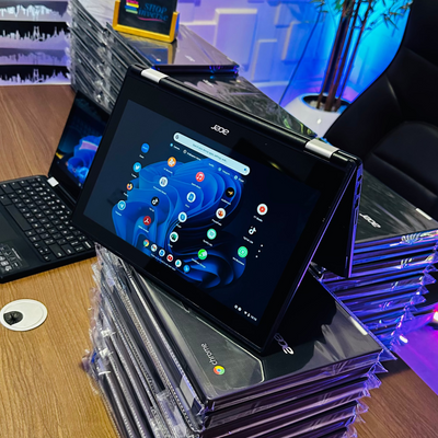 A stack of Acer Chromebook R11 laptops with one laptop open displaying the Chrome OS interface. The laptops are black and appear to be in a retail or commercial setting.