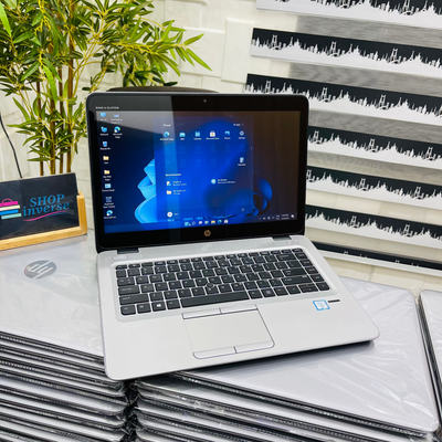 Open laptop on a stack of HP laptops with a plant and striped wall in the background