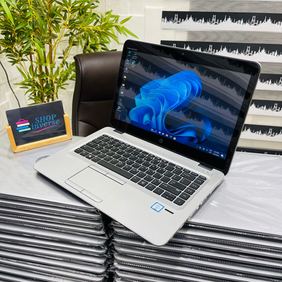 Laptop on a stack of similar laptops with a plant and 'Shop Universe' sign in the background